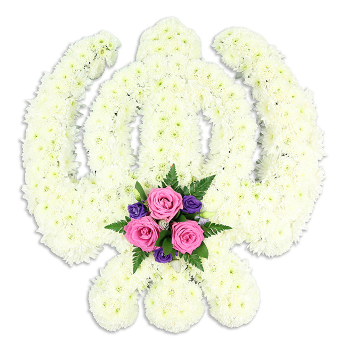 A reverent floral interpretation of the Sikh Khanda symbol dominates the image, set crisply against a flawless white backdrop so that every detail of the tribute is clearly defined. The entire emblem - the upright double-edged sword in the centre, the perfectly rounded Chakra encircling it, and the two protective Kirpans sweeping outwards on either side - is composed of countless small white chrysanthemum heads. Each bloom is tightly nestled to the next, creating a continuous, cushion-like surface with a soft, velvety sheen. The flowers appear freshly cut, their petals slightly curved and full, suggesting the cool touch and gentle fragrance you might notice when a tribute first arrives from a trusted New Southgate florist. At the base of the central sword, where the lower blades converge, a compact cluster of coloured flowers forms a deliberate focal point. Three pink roses, generous in size and at the peak of their opening, rest at the heart of this accent, their petals layered in concentric spirals. Around them, smaller deep purple blooms - perhaps freesias or lisianthus - introduce a richer tone, while dark green fern fronds and leaves weave through the cluster, adding structure and contrast. The lighting is bright yet soft, casting a faint halo of shadow beneath the tribute that suggests it is gently elevated from the surface. This custom Khanda arrangement, crafted with careful attention to Sikh symbolism and family traditions in North London, would be fitting for a Sikh funeral service, celebration of life, or memorial at a local gurdwara near New Southgate. It carries an air of solemn beauty, offering comfort, honour, and a visible expression of spiritual devotion and remembrance.