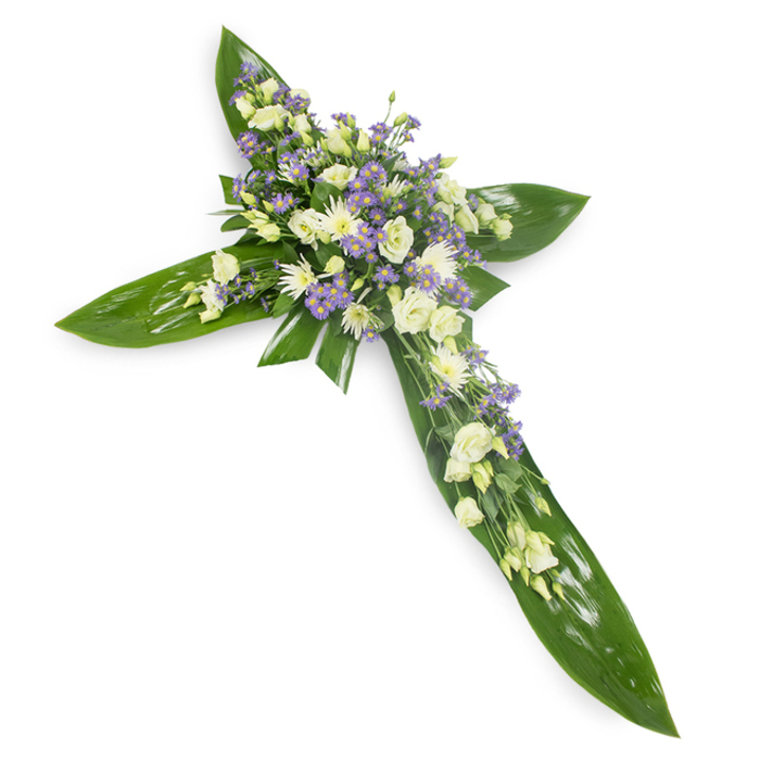 An intimate, reverent cross arrangement captured from a slightly elevated view on a stark white surface, every element chosen to convey calm and respect. The structural framework is composed of broad, verdant leaves - large tropical blades whose glossy sheen and visible veins create a stable, green lattice for the floral work. At the centre and extending along the vertical and horizontal arms is a generous grouping of soft-toned flowers: creamy-white lisianthus with their gently unfurling layers, clustered white daisy-like chrysanthemums providing rounded highlights, and numerous sprays of pale lavender star-shaped blooms, likely limonium or small asters, offering a tender purple counterpoint. Finer green sprigs are tucked through the massed flowers to add depth and a natural finish. The lighting is diffused and neutral, bringing out the creamy warmth of the ivory blooms and the cool whisper of lavender without casting harsh shadows; the overall scent would be understated and clean, with grassy and sweet floral notes. Designed as a traditional sympathy or memorial piece, this cross is meant to read as both an emblem of faith and a comforting presence at funerals, wakes or memorial services. A florist from the New Southgate area would select these seasonal varieties to suit services at local venues - from parish churches to the cemeteries near Friern Barnet - where its gentle palette and careful craftsmanship offer solace and a graceful tribute to a life remembered.