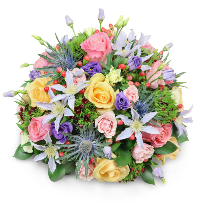 A generously rounded floral bouquet sits against a bright white background, the smooth backdrop making each flower, berry, and leaf appear almost three-dimensional, as though you could reach out and touch the petals from a living room in New Southgate. The bouquet forms a compact dome, densely packed with roses, clematis, lisianthus, sea holly, and mixed foliage, all arranged with the careful hand of an experienced florist. At the forefront are garden roses in soothing tones of soft pink, golden yellow, and delicate peach, their plush petals swirling in layered curls that create a sense of softness and romance. Nestled among the roses are several star-shaped clematis flowers in shades of white, lavender, and gentle violet, their slim petals radiating outward around pale or bright yellow centres, introducing a light, airy note that feels reminiscent of cottage-style gardens you might glimpse near Arnos Park. Standing slightly above the rounded surface of the bouquet are a few blue eryngium stems, their spiky, metallic heads adding a bold, textural contrast that breaks the bouquet's smoothness in a considered way. Deeper purple lisianthus scatter through the arrangement, some still closed in ruffled buds, others relaxing into open, cup-like blooms that intensify the richer tones. Tiny, vivid red hypericum berries are dotted throughout, like drops of lacquered colour that catch and reflect the soft studio light. All of this is anchored by a lush bed of greenery, from wide, glossy leaves to light, feathery sprigs and glimpses of darker, burgundy-tinted foliage, creating depth and a natural, just-picked-from-the-garden impression. The overall mood is joyful yet graceful, making this bouquet a fitting choice for celebrations, thoughtful get-well wishes, or simple everyday appreciation within the New Southgate community.
